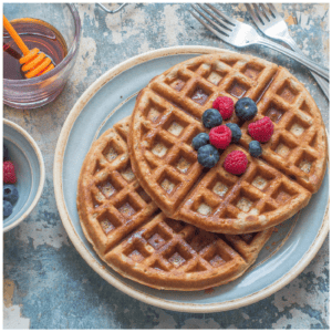 Two waffles with fruit topped on it.