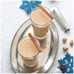 Two glasses of ponche de creme with cinnamon sticks on top.
