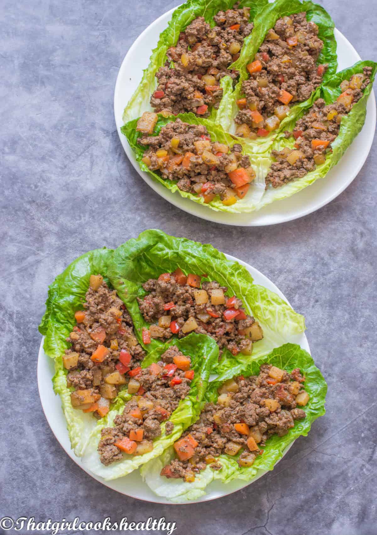 Two plates of wraps with ground beef on a bed of lettuce.
