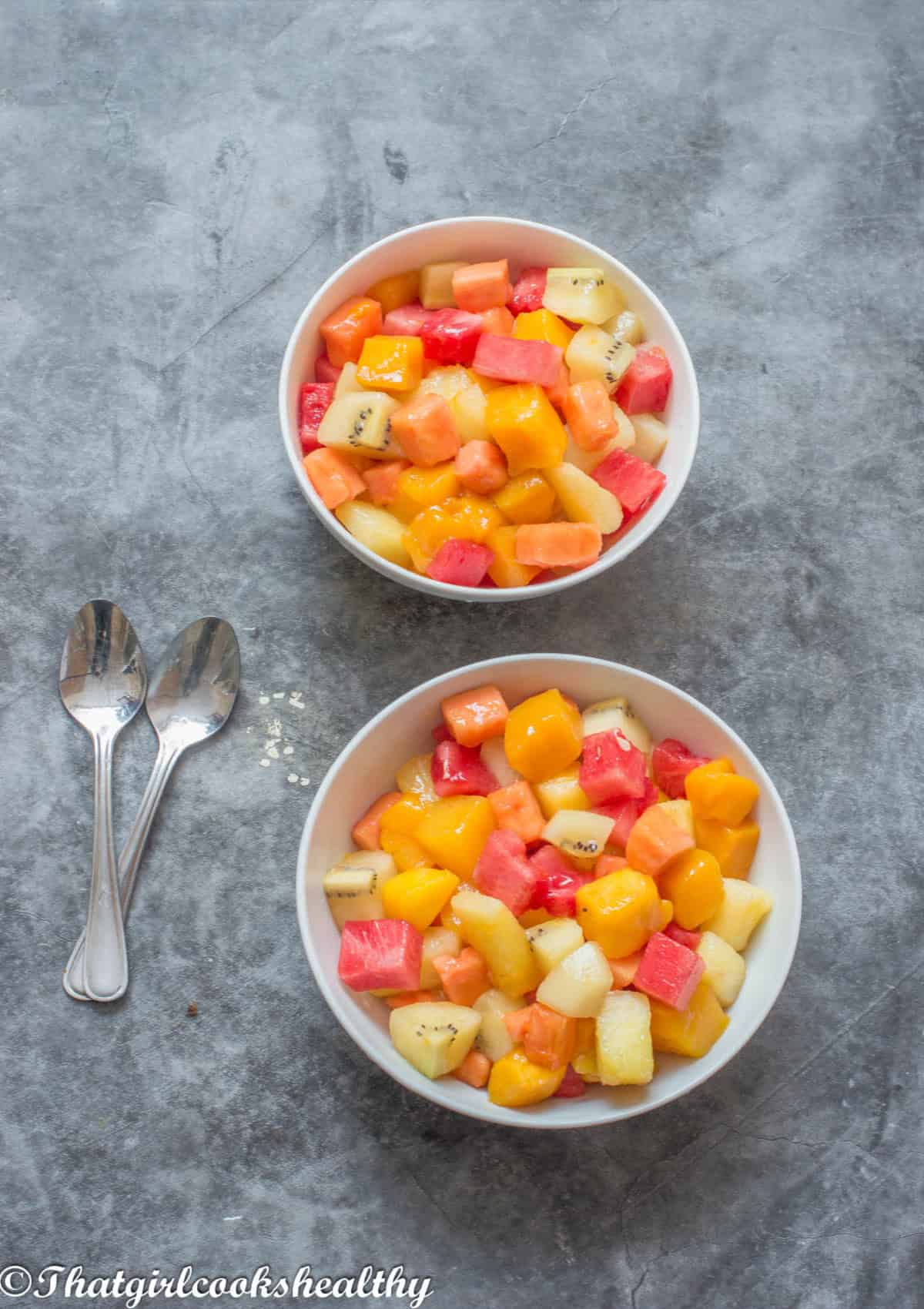 2 bowls of fruit salad with small spoons