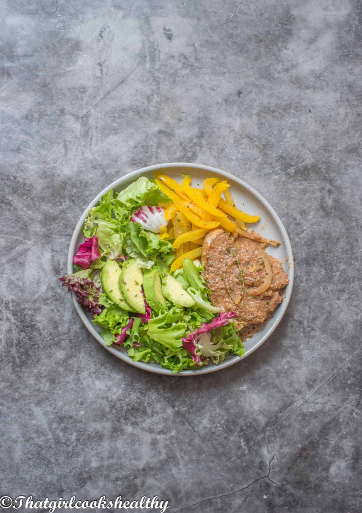 A single plate of tuna steak, peppers, avocado and fresh salad