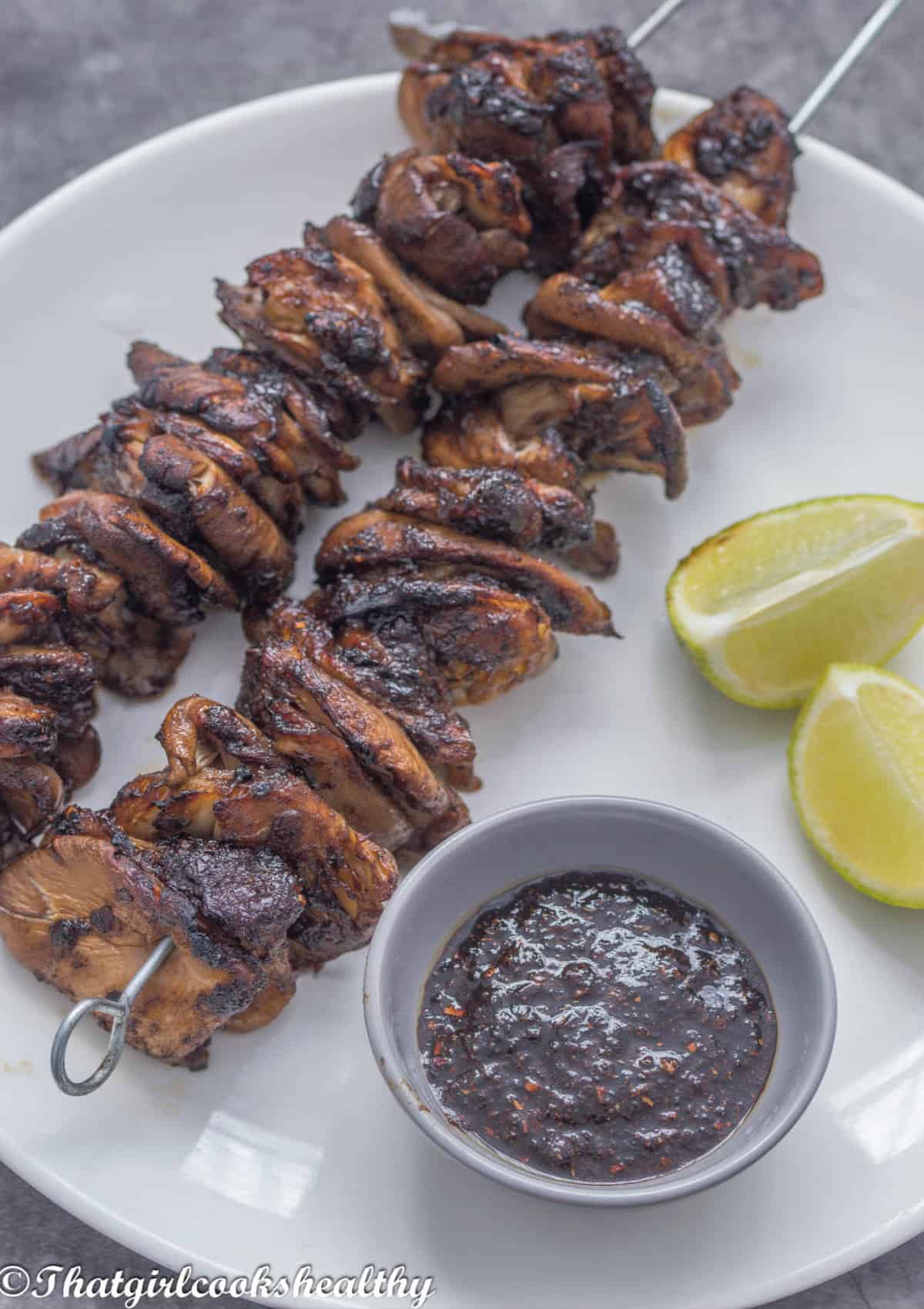 Close up of 2 jerk oyster mushrooms on a skewer with lime and sauce