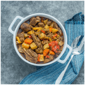 pieces of lamb with vegetables in a white casserole dish