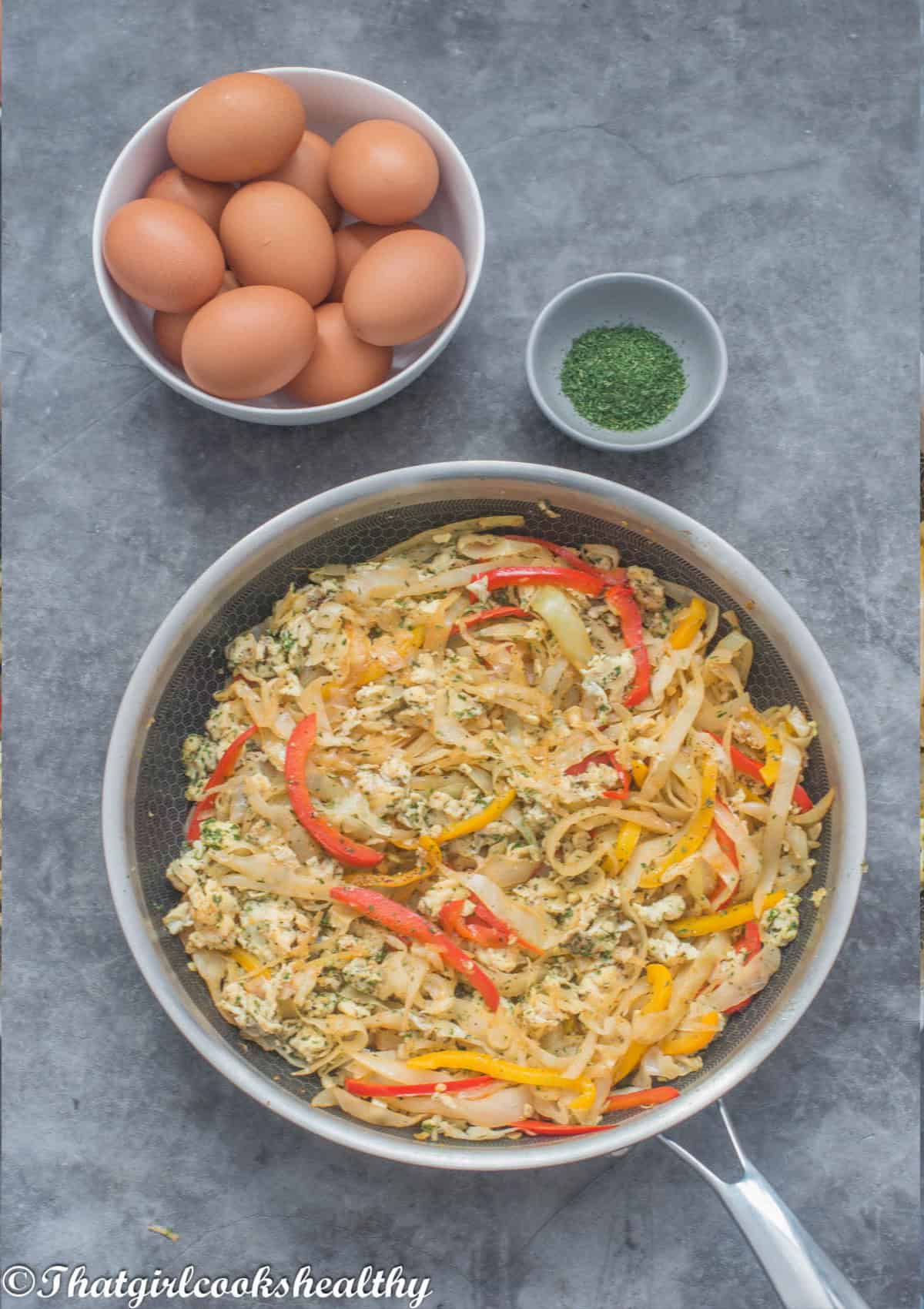 eggs and cabbage in a skillet with fresh eggs in a bowl with a dish of parsley